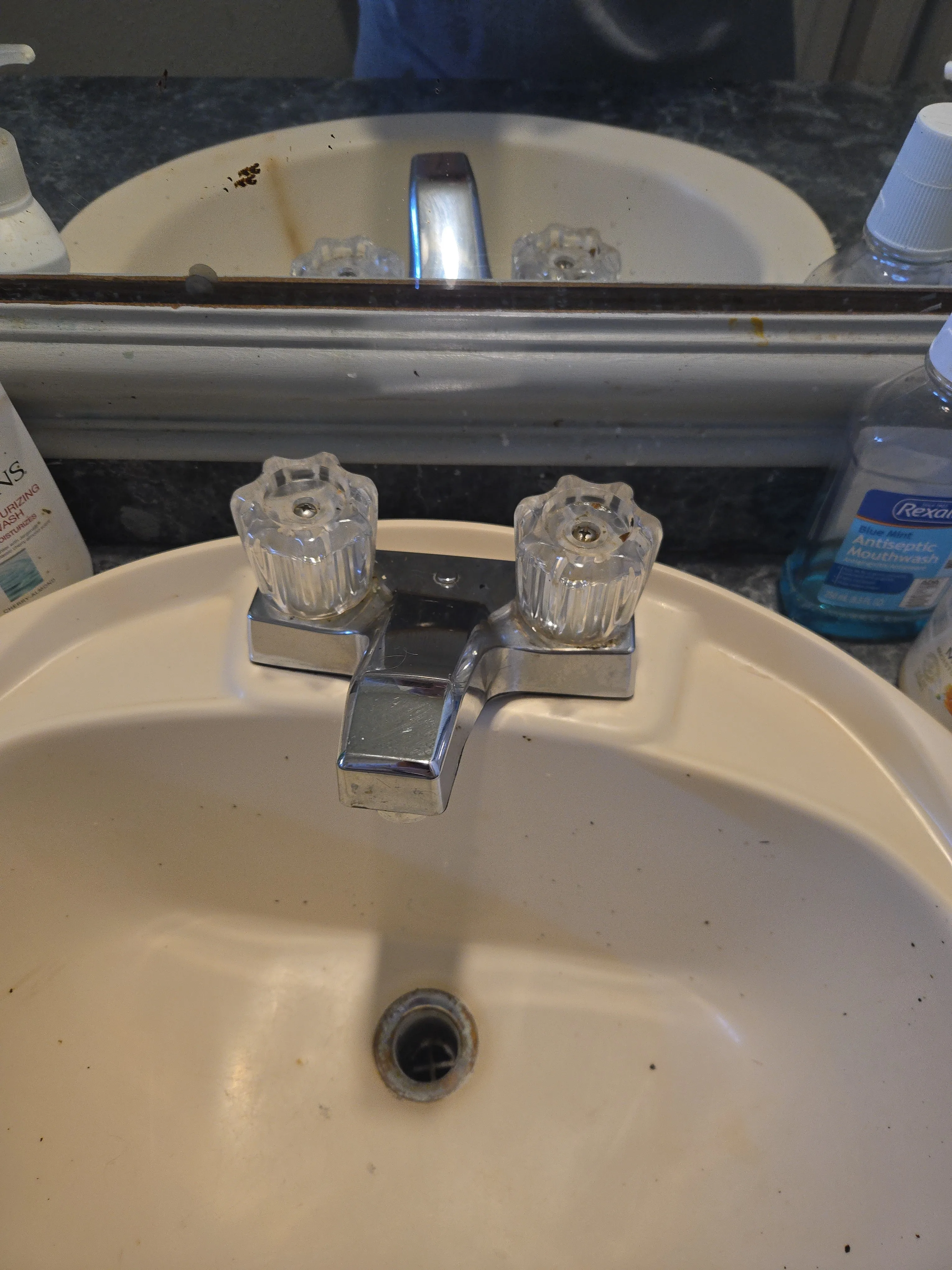 Bathroom sink after cleaning with the faucet reset while the existing stain in the mirror still shows through