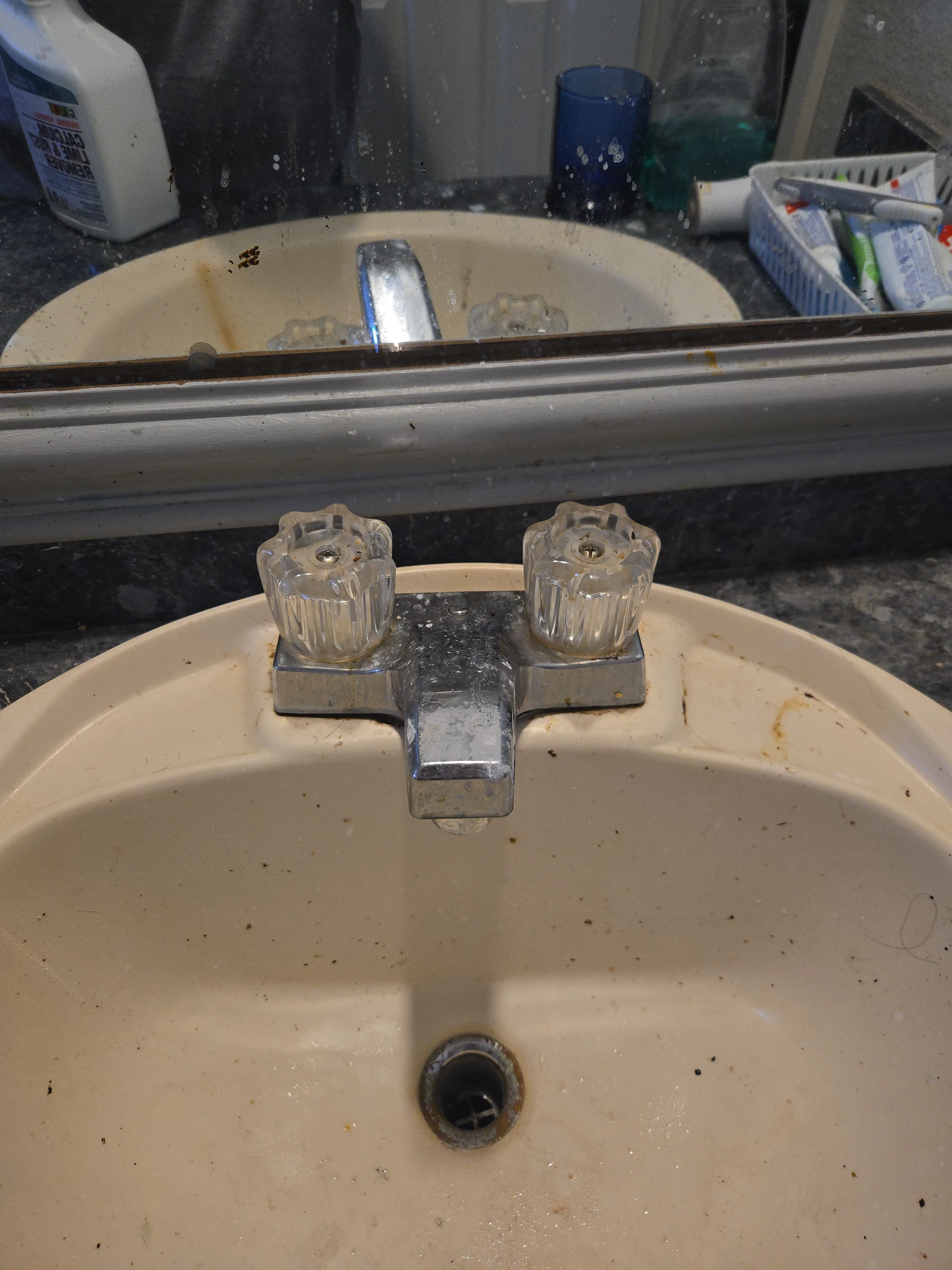 Bathroom sink before cleaning with residue on the faucet, basin, and mirror edge